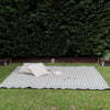 Outdoor setting with a patterned blanket on grass against a hedge.