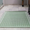 Green patterned rug on a tiled floor with a plant and furniture in the background.