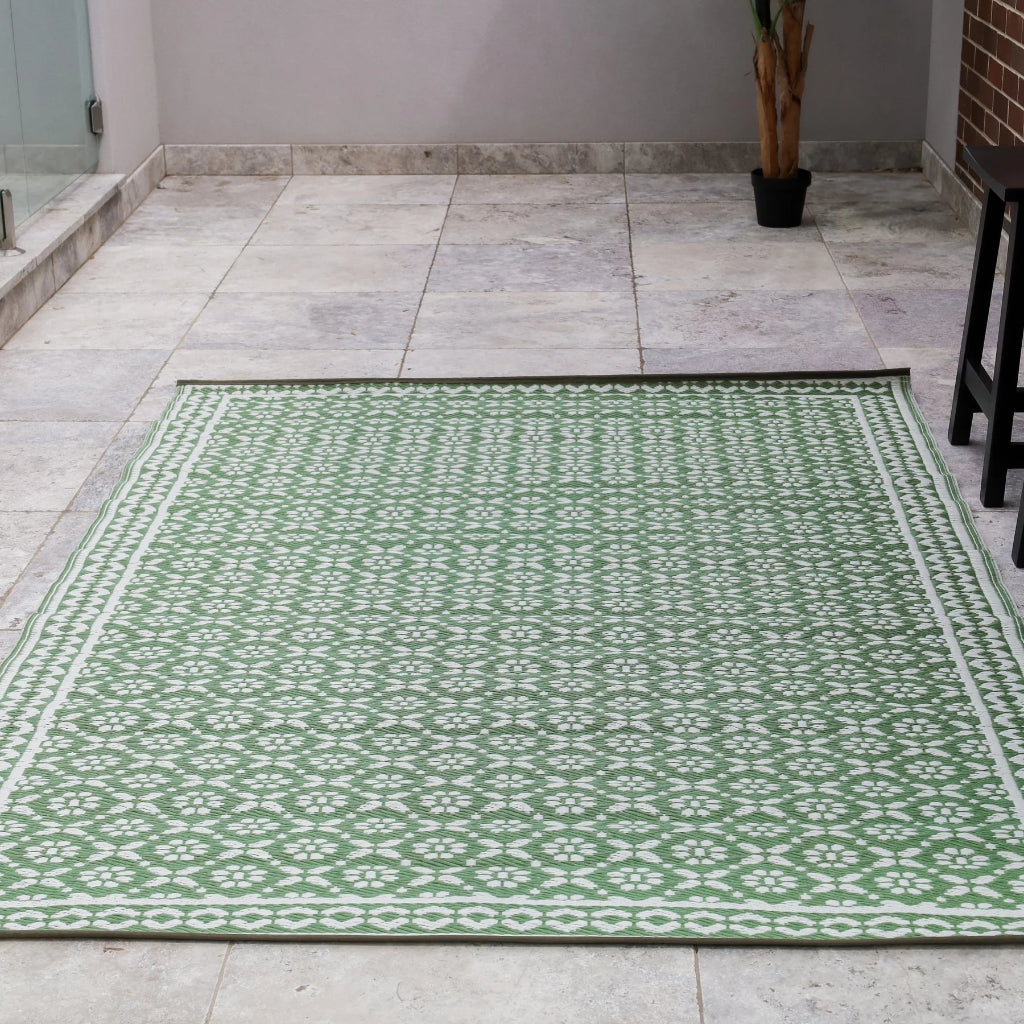 Green patterned rug on a tiled floor with a plant and furniture in the background.